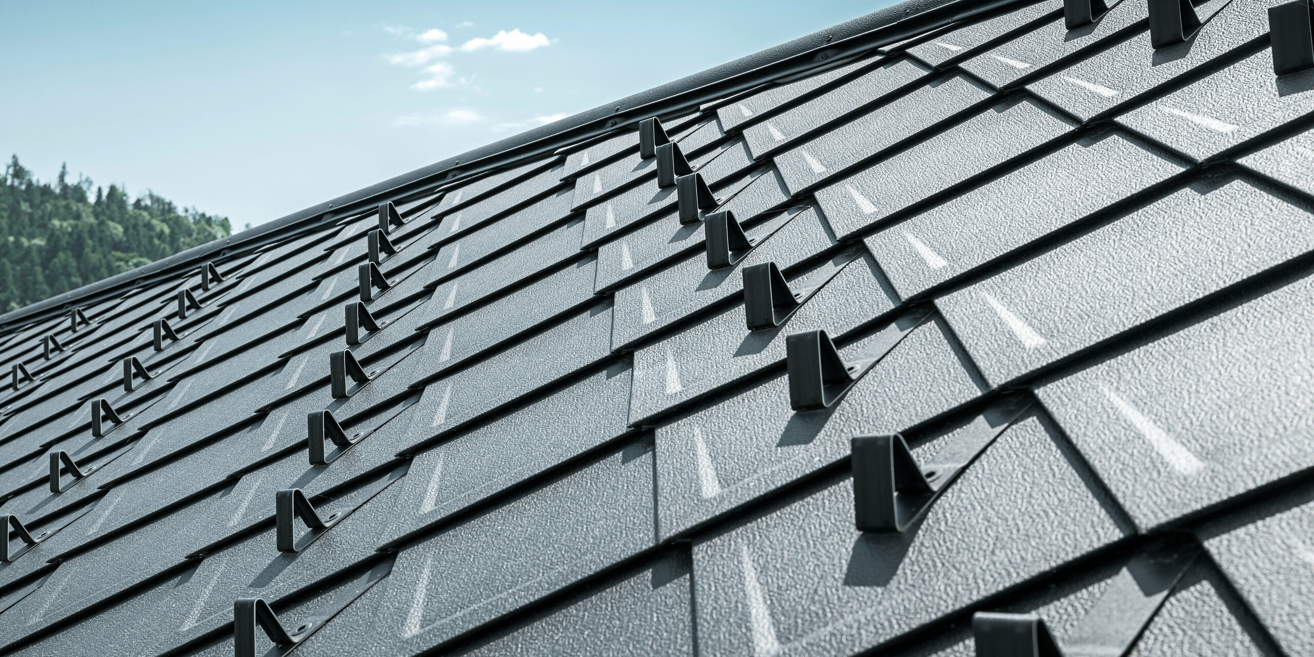 Nahaufnahme des Daches eines traditionellen Einfamilienhauses in Stara Bystrica, Slowakei, eingedeckt mit widerstandsfähigen PREFA Dachrauten 29 × 29 in der Farbe P.10 Schwarz. Die langlebige Aluminiumdeckung in eleganter Schuppenoptik zeigt integrierte Schneestopper, die für zusätzliche Sicherheit sorgen. Die klare Struktur und das moderne Design der Dachrauten verleihen dem Gebäude ein harmonisches und ästhetisches Gesamtbild.