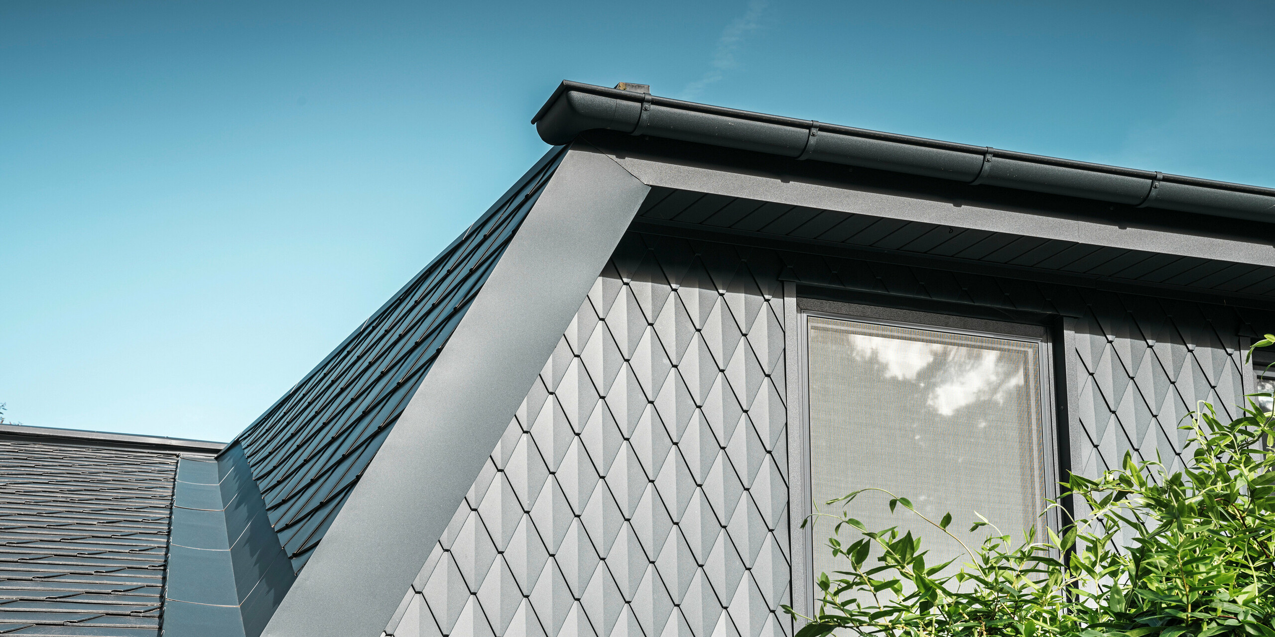 Trapesformet takvindu på en enebolig i Mechernich, kledd med små PREFA takrombe i P.10 antrasitt. Taket er dekket med PREFA takhingel DS.19 i samme farge. Den høykvalitets aluminiumsbekledningen sørger for værbestandighet og et moderne, estetisk utseende.