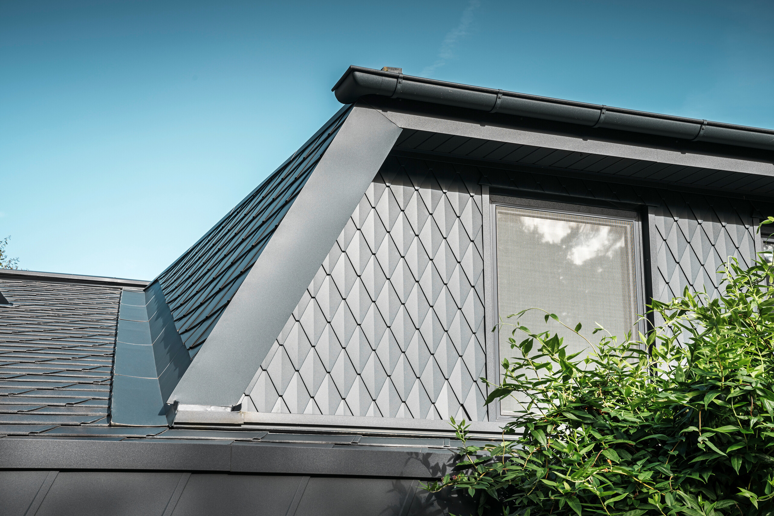 Trapesformet takvindu på en enebolig i Mechernich, kledd med små PREFA takrombe i P.10 antrasitt. Taket er dekket med PREFA takhingel DS.19 i samme farge. Den høykvalitets aluminiumsbekledningen sørger for værbestandighet og et moderne, estetisk utseende.