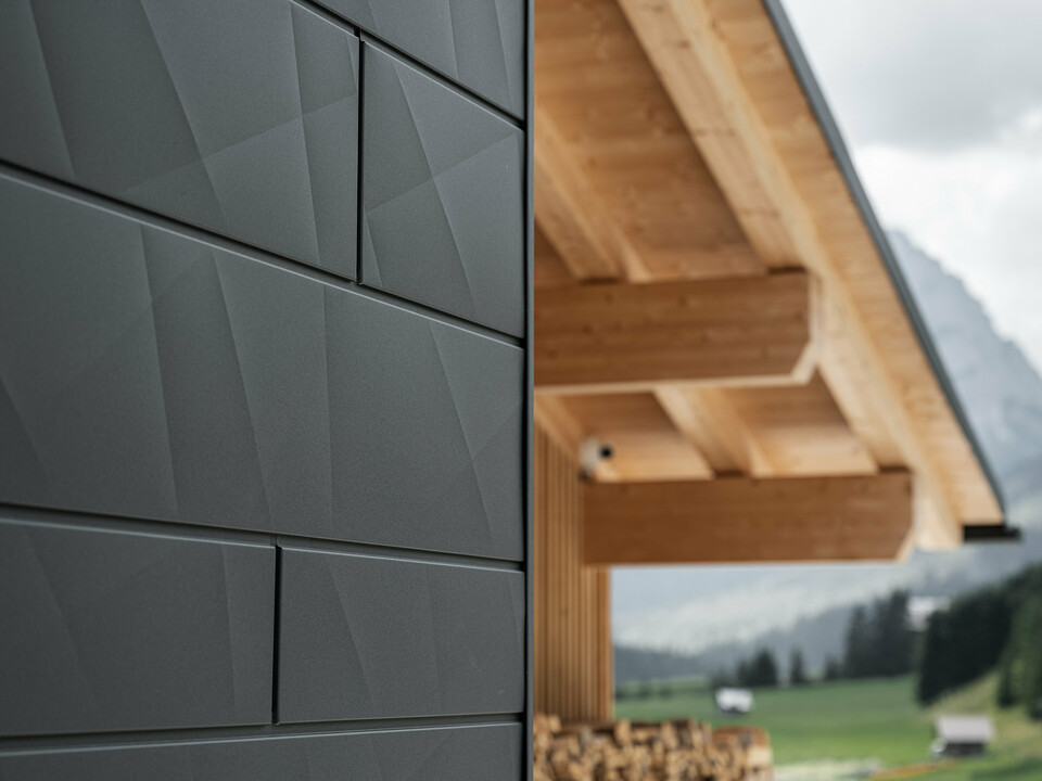 Nærbilde av Siding.X fasadeplater i P.10 svart fra PREFA på Casa Hoffe i Sappada, Italia. Fasadesystemet i aluminium er dyktig montert i et moderne, abstrakt design som danner en tiltalende kontrast til de synlige treelementene i takkonstruksjonen. Den innovative fasadeløsningen passer perfekt inn i det alpine miljøet og står for en kombinasjon av funksjonalitet, holdbarhet og estetisk byggekultur.
