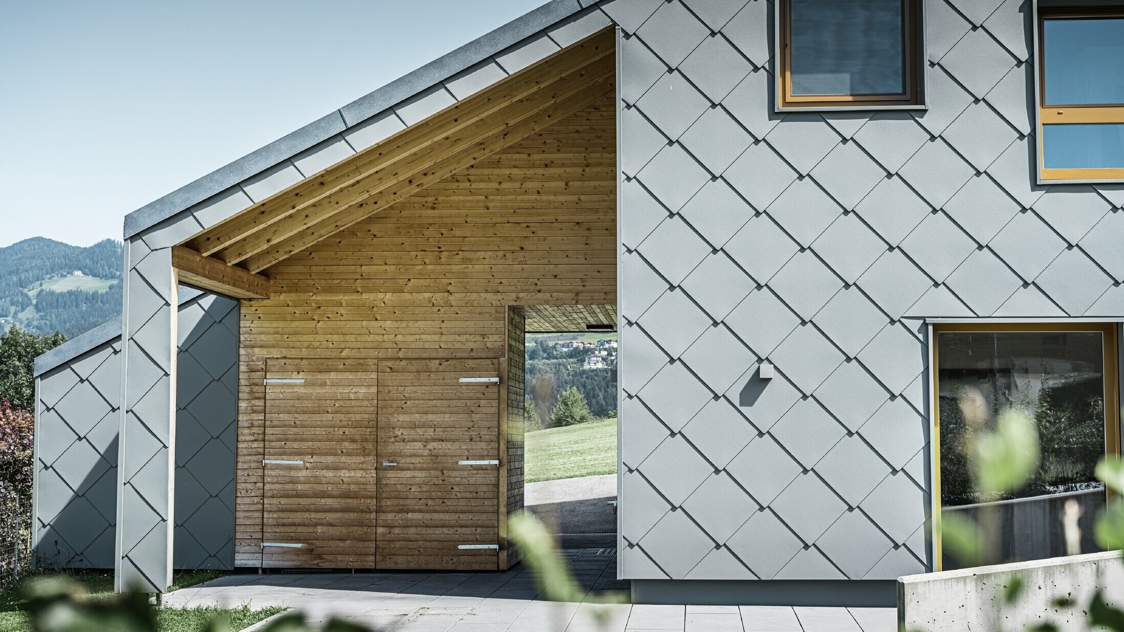 Inngangsområdet med tak har vannrett trekledning, resten av fasaden er kledd med den store PREFA veggromben i aluminium i lysegrått