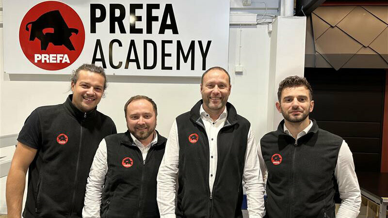 Das PREFA Academy Team in Skien sowie der Country Manager von Norwegen, die in ihren PREFA-Westen vor dem PREFA Academy Logo posieren.