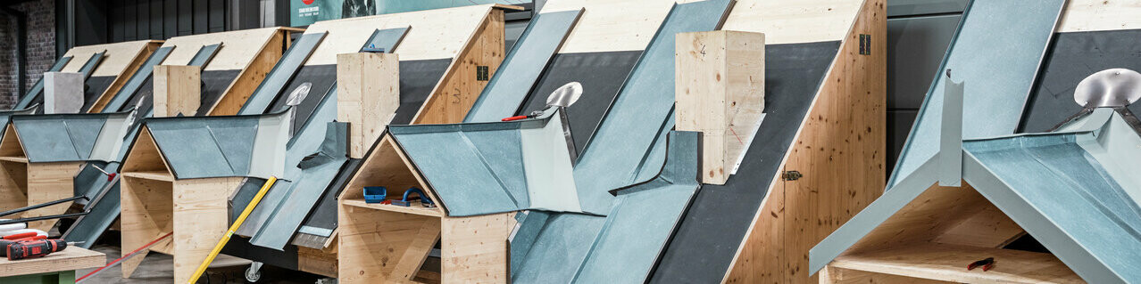 Innenräume des PREFA Schulungszentrums in Rheinbach (DE). Hier stehen viele Dachmodelle, an denen die Schulungsteilnehmer die richtige Verlegung und Montage von PREFA Produkten üben können. Ein geschulter Lehrverleger steht ihnen dabei zur Seite. 