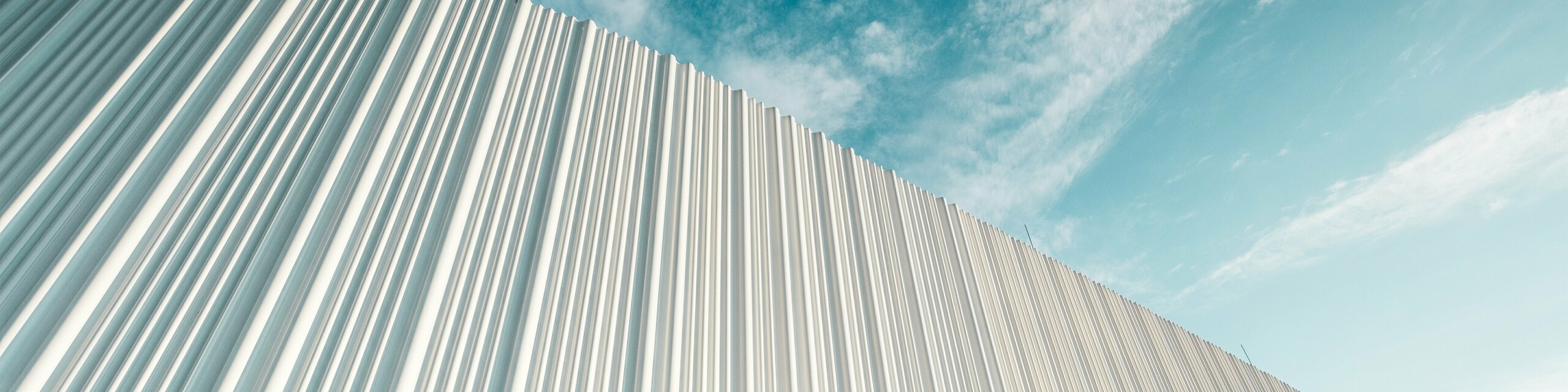 Atemberaubende Architektur mit weißer PREFA Aluminiumfassade im Walter Business-Park bei Wien. Die Fassade aus maßgefertigten Individualprofilen erzeugt durch ihren fließenden Wellencharakter ein faszinierendes Spiel aus Licht und Schatten. Drei unterschiedliche Profilformen sorgen für eine außergewöhnliche Tiefenwirkung und verleihen dem Gebäude eine stilistisch klare und zugleich dynamische Optik. Die langlebige, witterungsbeständige PREFA Oberfläche kombiniert moderne Ästhetik mit funktionaler Perfektion – ein echtes Highlight zeitgenössischer Fassadengestaltung, das architektonische Qualität und technische Raffinesse sichtbar macht.