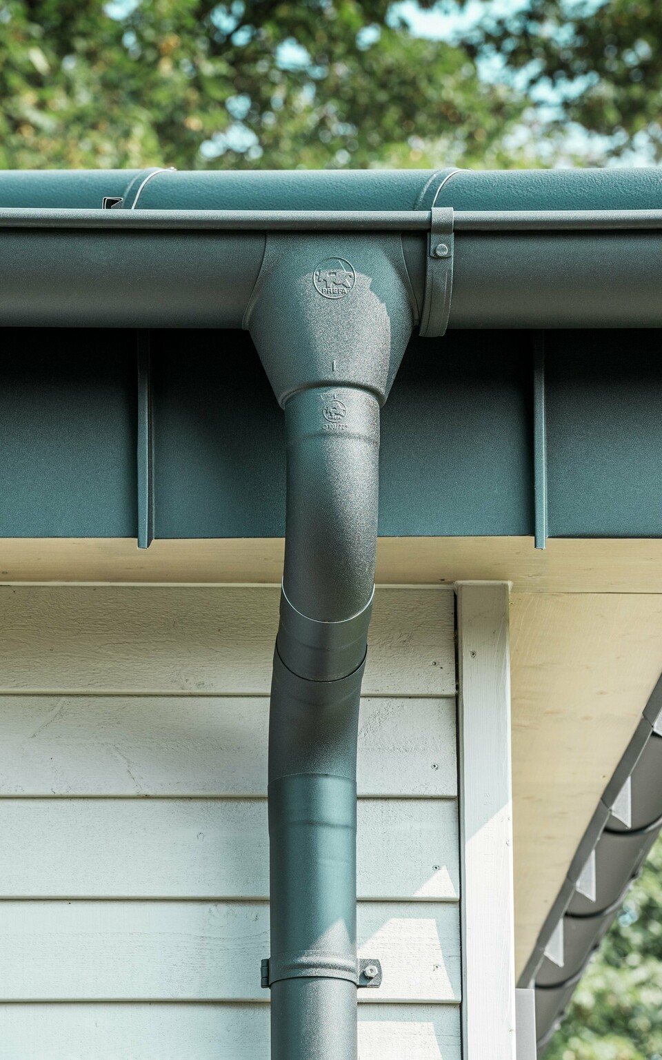Nahaufnahme der robusten PREFA Dachentwässerung eines Bungalows in Rommerskirchen. Die hochwertige Saumrinne und das Ablaufrohr in P.10 Schwarz bieten optimalen Schutz vor Witterungseinflüssen. Langlebigkeit und Funktionalität verbinden sich hier mit elegantem Design aus Aluminium.