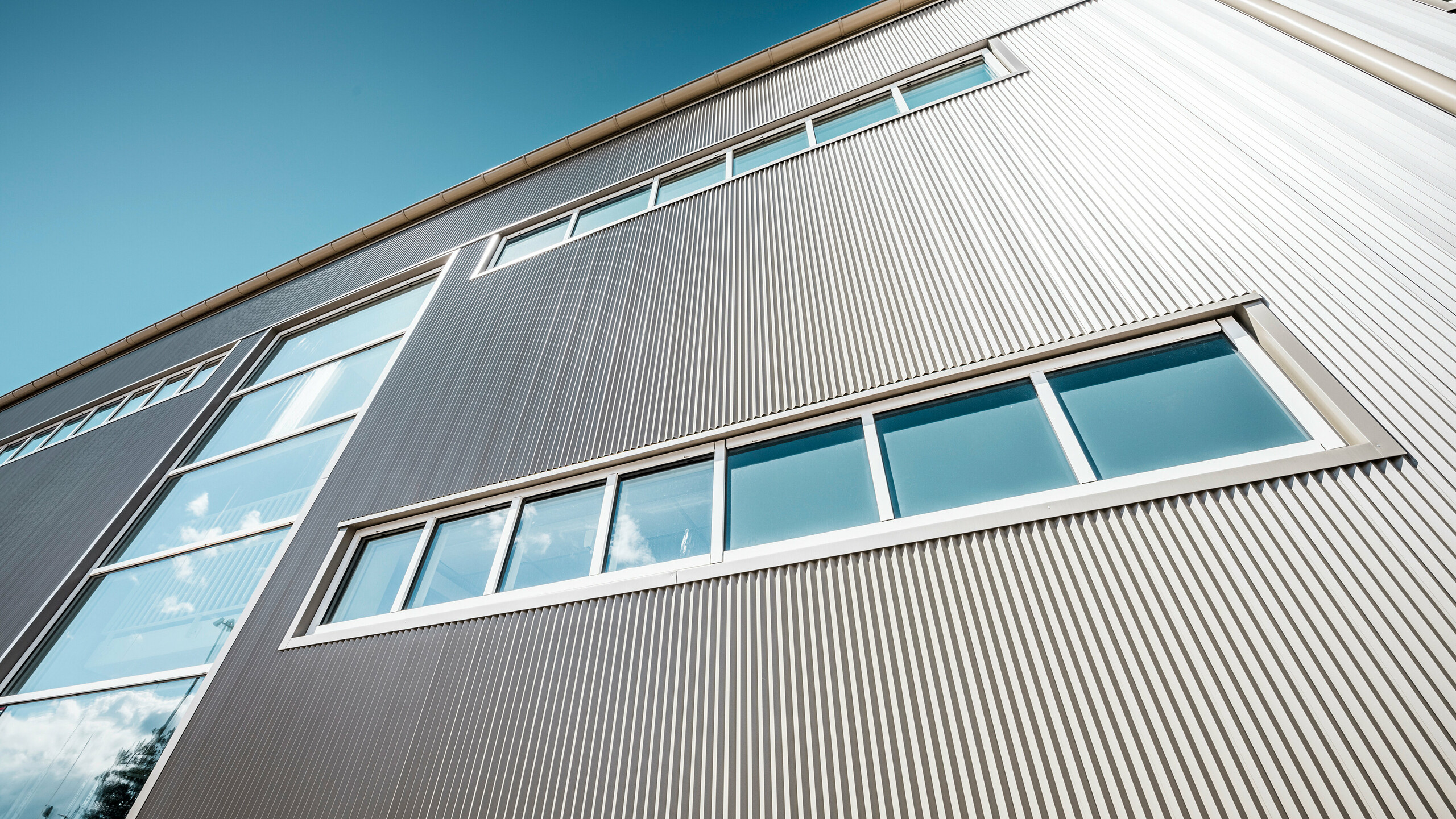 Utvendig utsikt over Park Arena i Värnamo, Sverige, med en moderne PREFA-fasade i bronse. De sikksakkprofilene i aluminium skaper markante lys- og skyggeeffekter. De innfelte vinduene passer harmonisk inn i den presist bearbeidede fasaden, som står for lang levetid, motstandsdyktighet og moderne design.