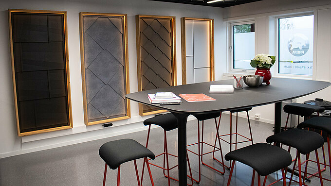 Innenansicht eines Raumes in der PREFA Academy in Skien, mit einer Präsentation von Fassaden- und Dachsystemen an der Wand. Im Vordergrund befindet sich ein moderner Stehtisch, auf dem Broschüren und Materialien ausgestellt sind. Der Raum ist minimalistisch und gut beleuchtet, mit einem modernen Design, das die Produkte von PREFA in den Mittelpunkt stellt.