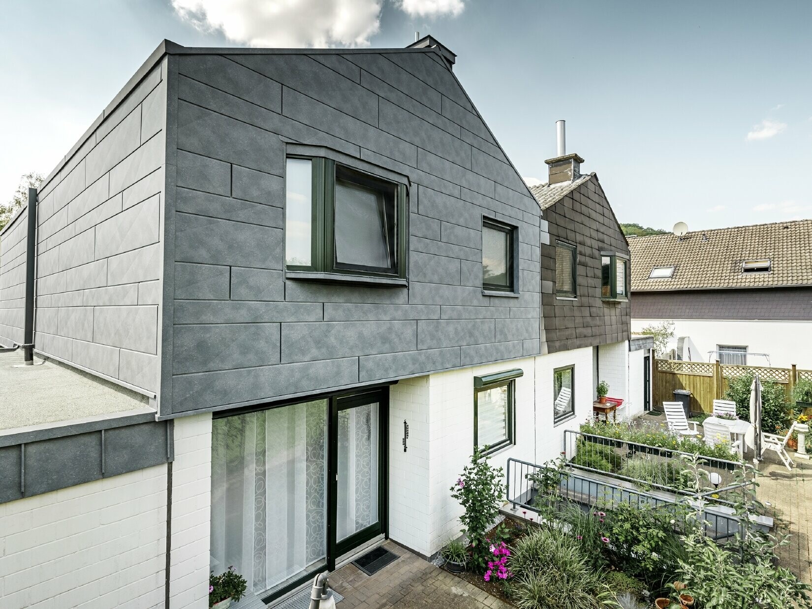 Den øvre delen av tomannsboligen ble renovert med fasadeelementet PREFA Siding.X i P.10 steingrå. Ved siden av vises husets andre halvdel før renoveringen – til sammenligning.