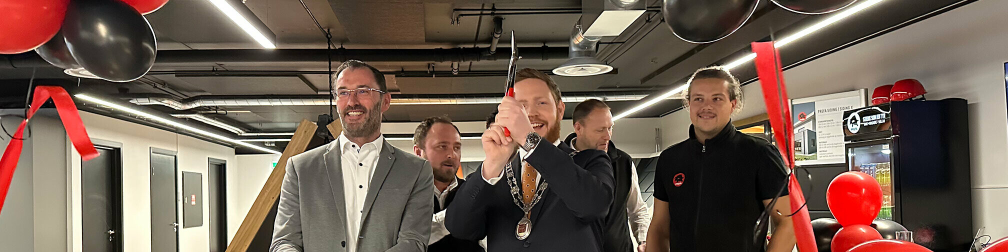 Berthold Ruck, technischer Leiter von PREFA, und der Bürgermeister von Skien beim Durchschneiden des Bandes zur feierlichen Eröffnung der PREFA Academy in Skien. Im Hintergrund sind das PREFA Academy Team aus Norwegen und PREFA Mitarbeiter zu sehen.