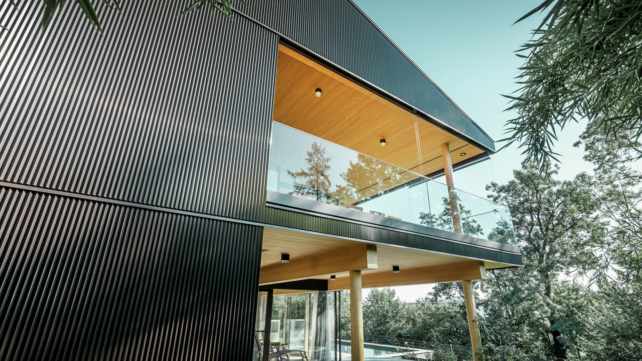 En enebolig sett fra siden, fasaden er kledd med mørk PREFA-sikksakkprofil. Man ser terrassen og en romslig balkong. Taket eller bjelkelaget er utformet med trepaneler.