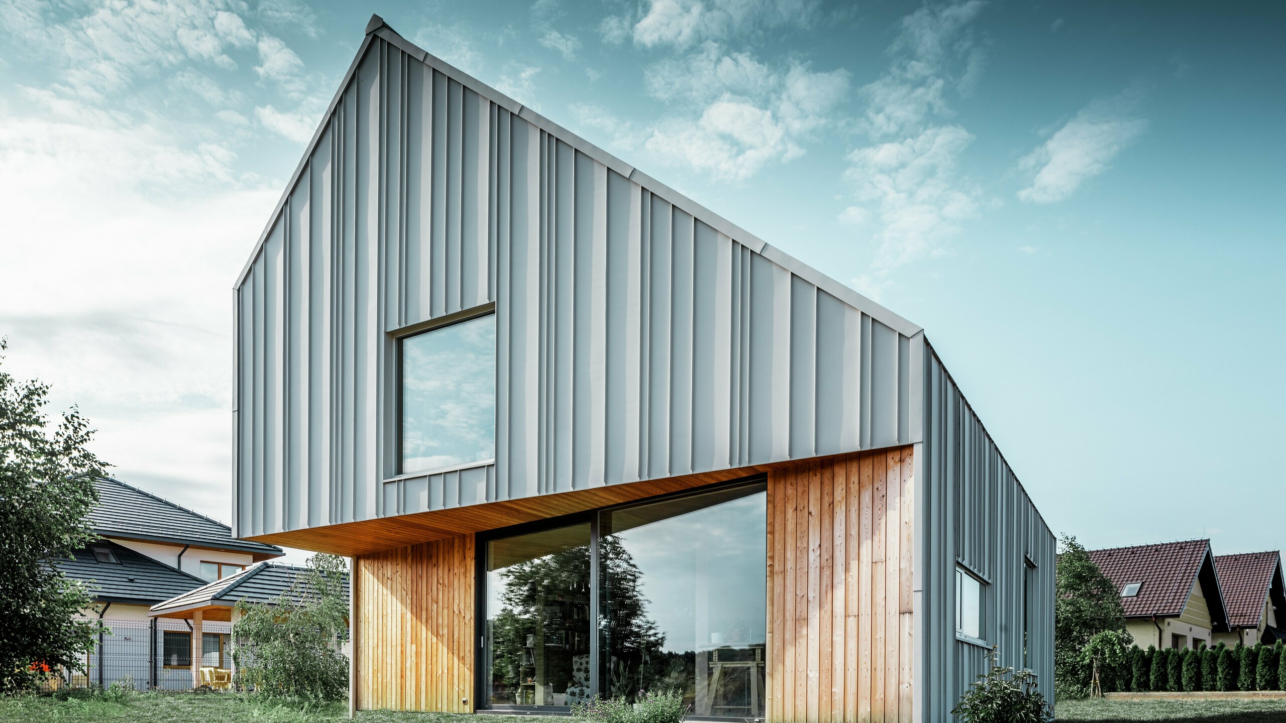 Moderne enebolig med skråtak uten takutstikk og aluminiumsfasade fra PREFA i hvitt. En trefasade er kombinert med vertikale trepaneler i første etasje. 