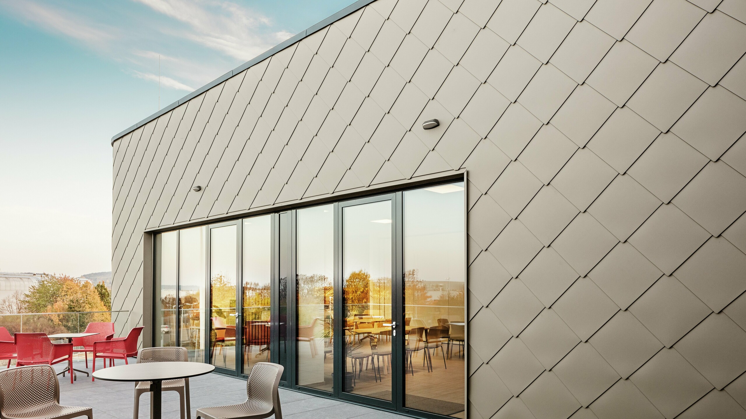 Die Fassade des neuen PREFA Standortes in Törökbálint besticht durch die eleganten PREFA Wandrauten 44 × 44 in P.10 Prefabronze. Die präzise verlegte Aluminiumfassade sorgt für ein modernes, dynamisches Erscheinungsbild und bietet gleichzeitig maximalen Schutz vor Witterungseinflüssen. Die großzügige Glasfront verbindet Innen- und Außenbereich und schafft auf der großzügigen Terrasse eine helle und einladende Atmosphäre.