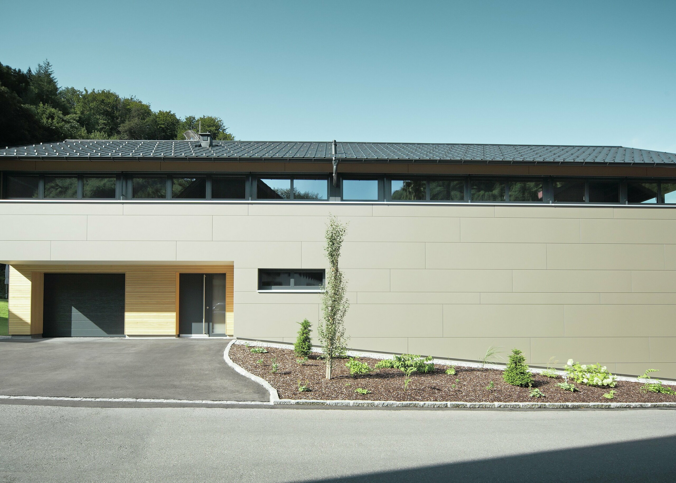 Hus med PREFA takpanel i P.10 antrasitt, kombinert med PREFA komposittpanel i bronse på fasaden; moderne byggestil kombinert med smale vinduer og trefasade.