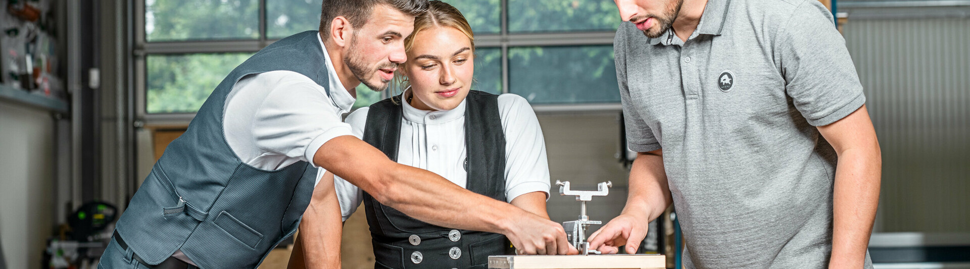 PREFA Anwendungstechniker Julian Eickhoff, Marvin Bürger von Bürger Falztechnik und Dachdeckermeisterin Fabienne Ellermeier schauen sich gemeinsam ein Lehrmodell in der PREFA Academy Rheinbach an. 