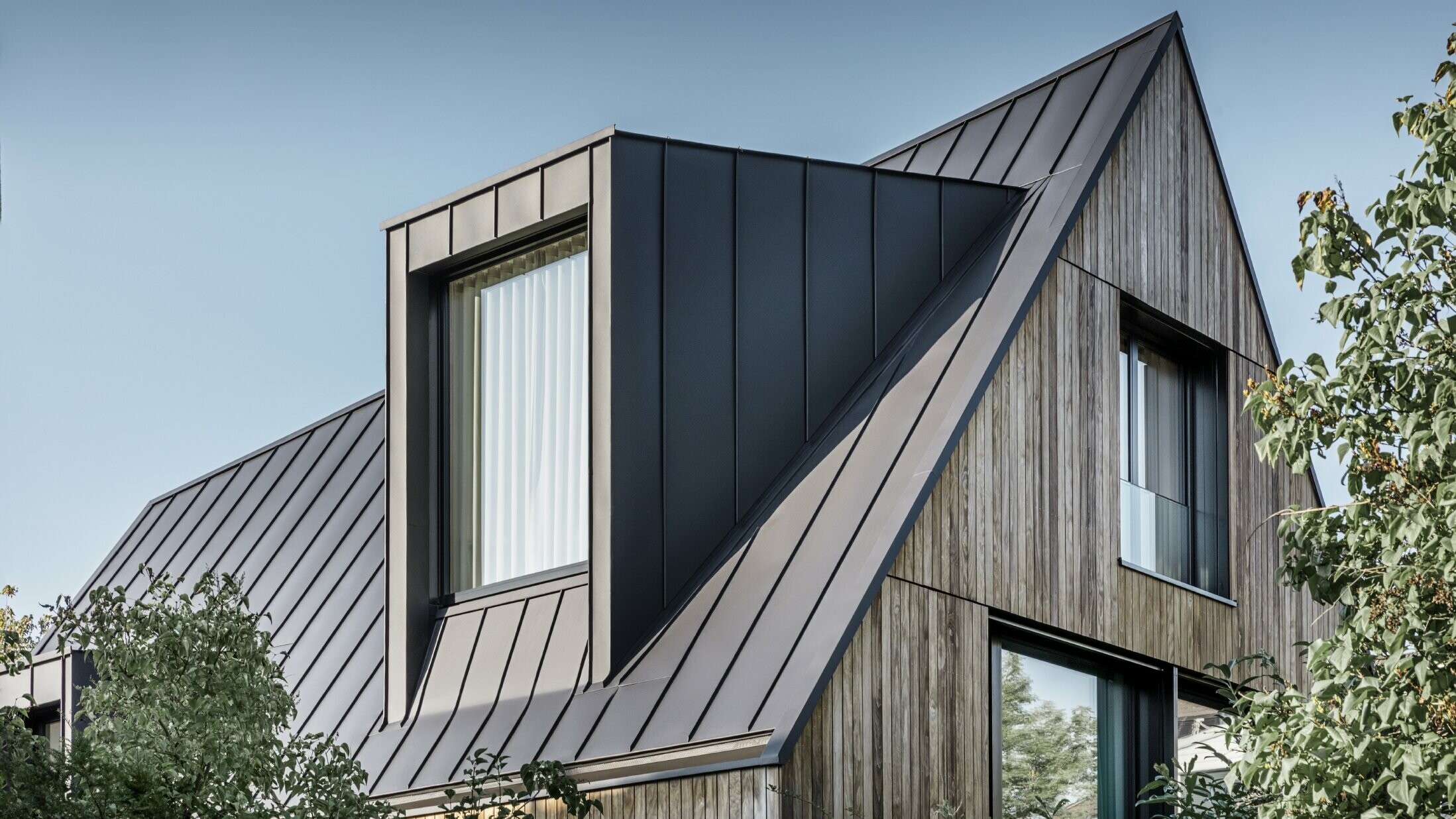 Bratt saltak med stort kvistvindu, tekket med PREFALZ fra PREFA i antrasitt, stående falstak kombinert med trefasade